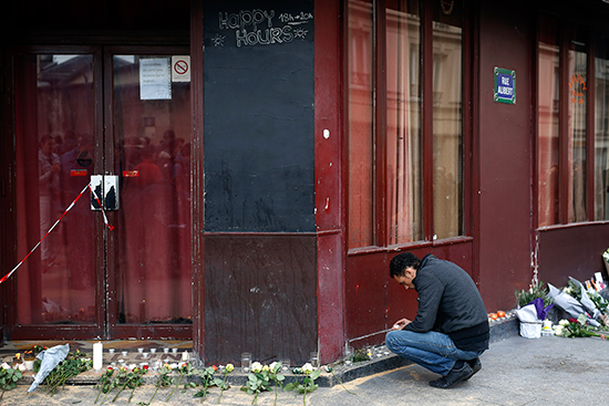 A man places a candle in front of the Carillon cafe in Paris Saturday Nov. 14, 2015, a day after over 120 people were killed in a series of shooting and explosions.