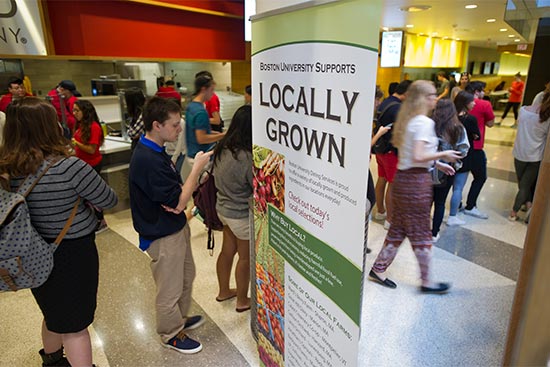 Boston University students file past a "Locally Grown" sign in a BU dining hall. BU Dining Services hit its goal of providing 20% sustainable food three years early.