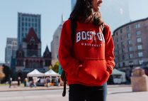 A Boston University student wearing a BU sweatshirt stands in Copley Square.