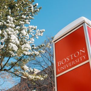Boston University sign with snow on top in front of a snowcovered tree