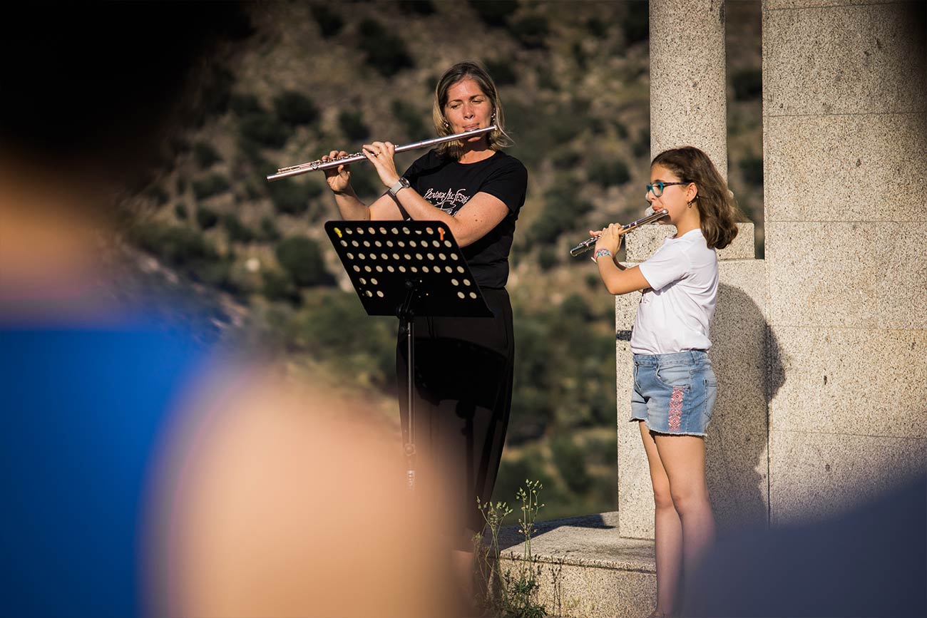 Full color slideshow photo of Bendada Music Festival Flute instructor Margarida Quitalo her student Beatriz Leal standing side by side in front of granite columns performing on a hilltop overlooking the village of Bendada.