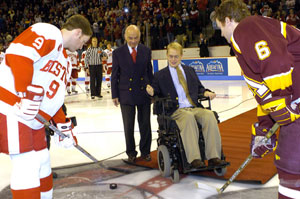 Former player Travis Roy (COM00), accompanied by President ad interim Aram Chobanian, drops the ceremonial first puck for Terrier captain Brian McConnell (MET05) (left) and Minnesota captain Judd Stevens. Photo by Rob Klein.