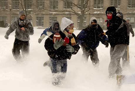 Three feet high and rising. Snowflakes and swirling winds were battering the Charles River Campus on January 23, when these students gathered at Alpert Mall for a cold game of football. Photo by Kalman Zabarsky.