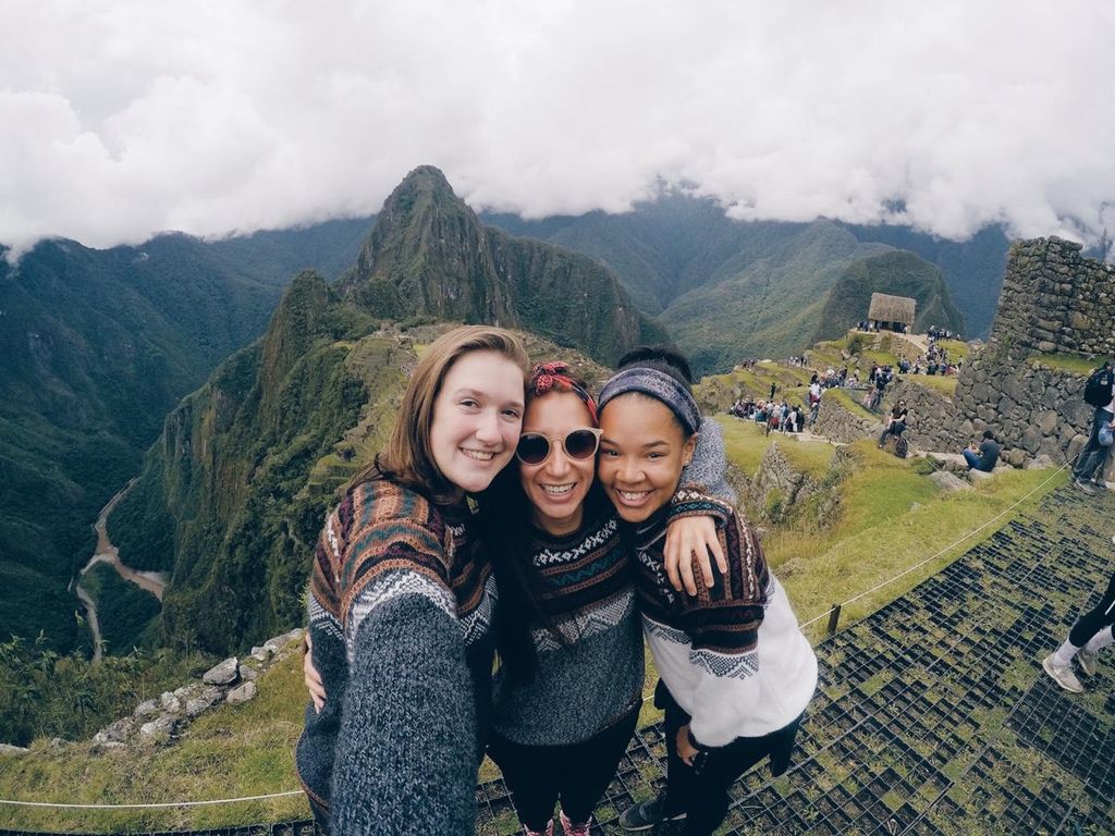 Jayda and two friends with a green mountain and stone walls behind them