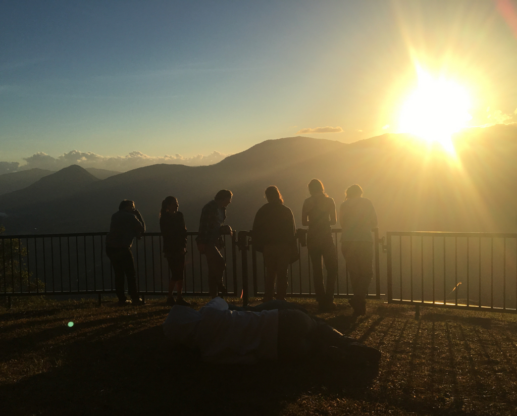 Six young people look out at the mountains and the sun setting behind them