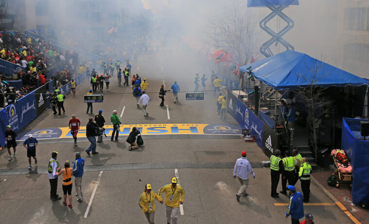 Shot above finish line during Boston marathon bombing. Smoke drifts overhead as people scatter.