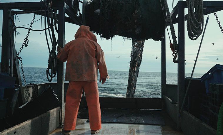 Back view of fisherman wearing orange rain gear on a fishing boat.