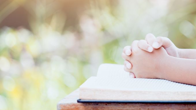 Child folding hands over book