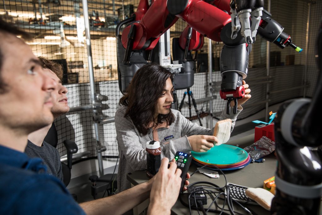 Female student working with robots hand so it can hold an object, while other students work on controlling other aspects of the robot