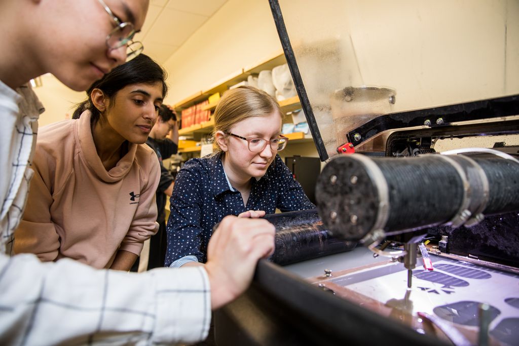 Group of Engineering students gathered around a machine that's cutting out their prototype