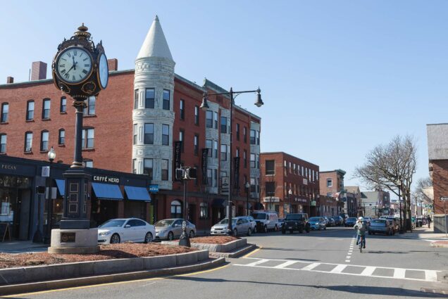 Photo of Washington Street in Brighton Center with old fashioned clock on the left; a biker rides down the street on the right.