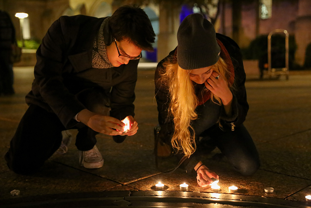 Boston University students Sam Desoto (CFA'19) (left) and Ashley Perry (CFA'19) light candles during a vigil on Marsh Plaza in memory of the victims of the Paris attacks. Photo by Chenyao Xu