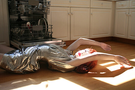 mannequin wearing a silver dress laying on kitchen floor in front of an open dishwasher