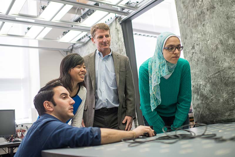 Postdoc researcher Michael Rahaim (ENG 15), PhD candidate, Emily Lam, Dr. Tom Little, Professor of Electrical and Computer Engineering and PhD candidate Iman Abdalla work in a lab on Thomas Little's smart lighting research with Lighting Enabled Systems & Applications Engineering Research Center (LESA ERC)