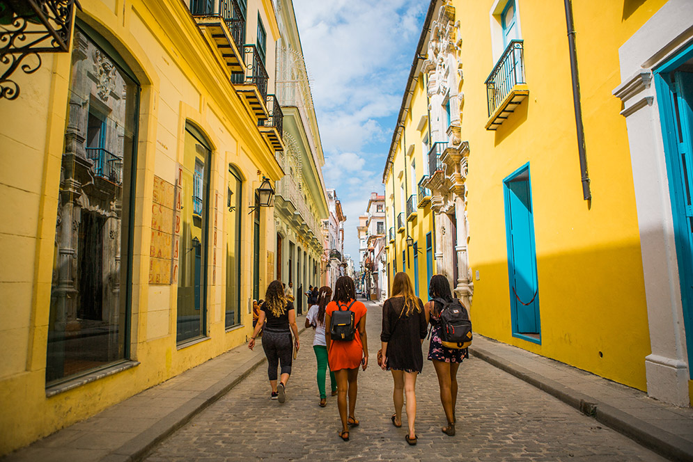 Boston University study abroad students walk down a street lined with yellow buildings in Old Havana, Cuba