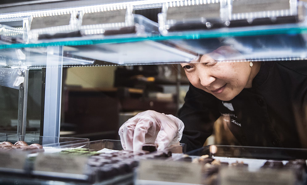 EHChocolatier founder Elaine Hsieh places an artisan chocolate in a display case in the company's Somerville store