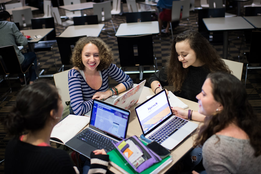 The four female founders of SquinchMag.com sit around a table.