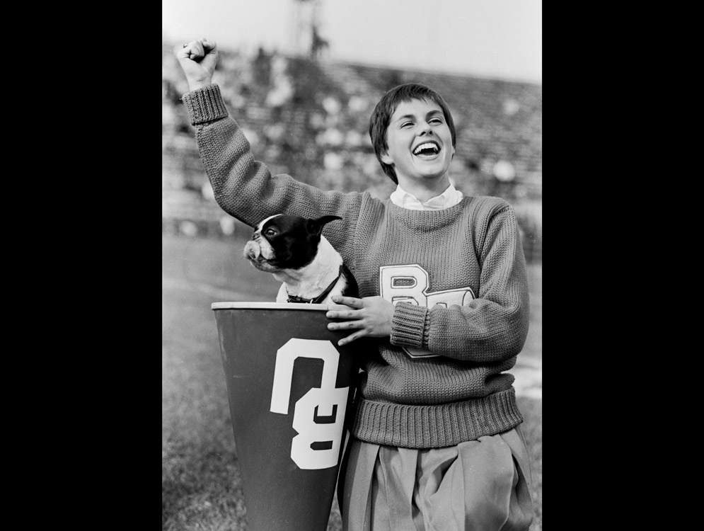 A cheerleader holds Rhett the Terrier, BU mascot, during a football game in 1960