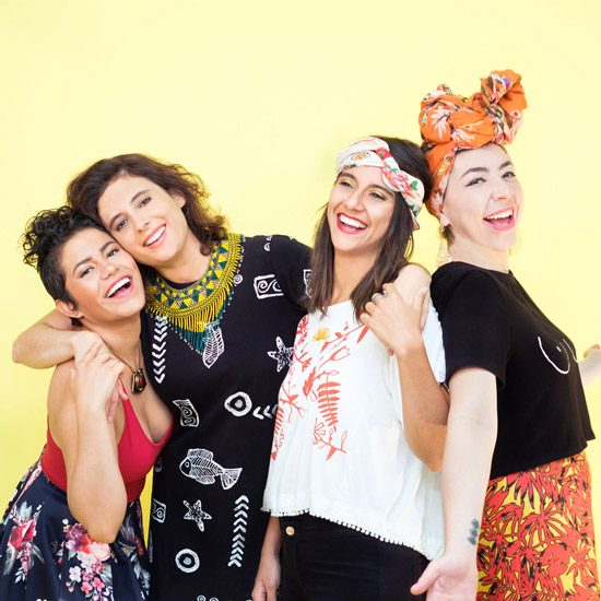 The female group, LADAMA, pose for a photo wearing loud clothing with a yellow background