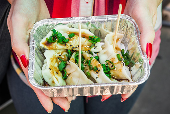 A woman wearing a red shirt and red nail polish holds a tray of gyoza dumplings street food.