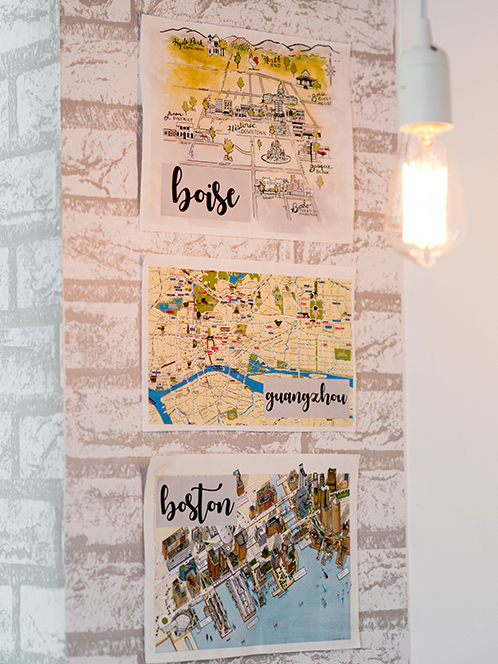 Illustrated maps of three different locations--Boise, ID; Boston, MA; Guangzhou, China--hang on a faux brick wall.