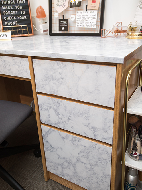 A brown wooden desk with drawers and tabletop covered with removable white marble contact paper.