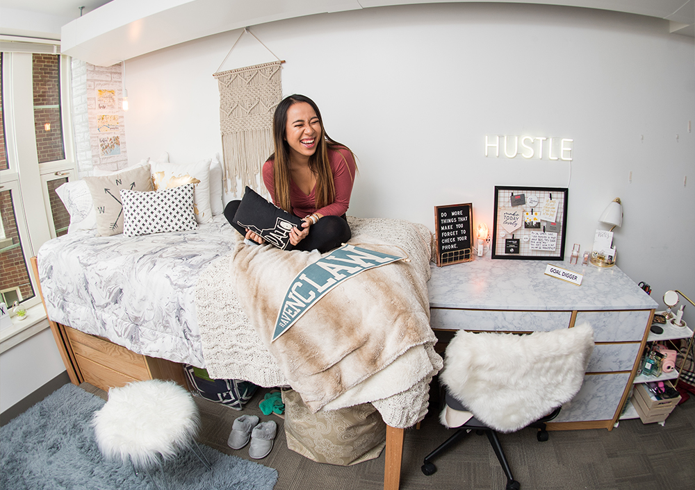 Boston University student Geneve Lau sits crosslegged on her dorm room bed laughing.