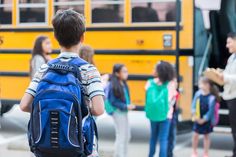 A child watches as students get on a yellow school bus