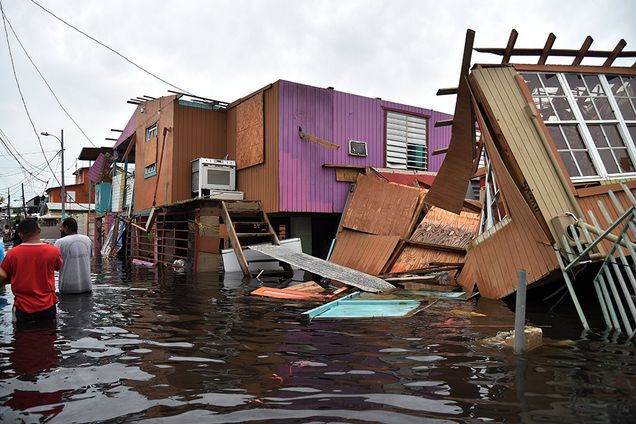 People walk in a flooded street next to damaged houses in Juana Matos, Catano, Puerto Rico, on September 21, 2017, after Hurricane Maria