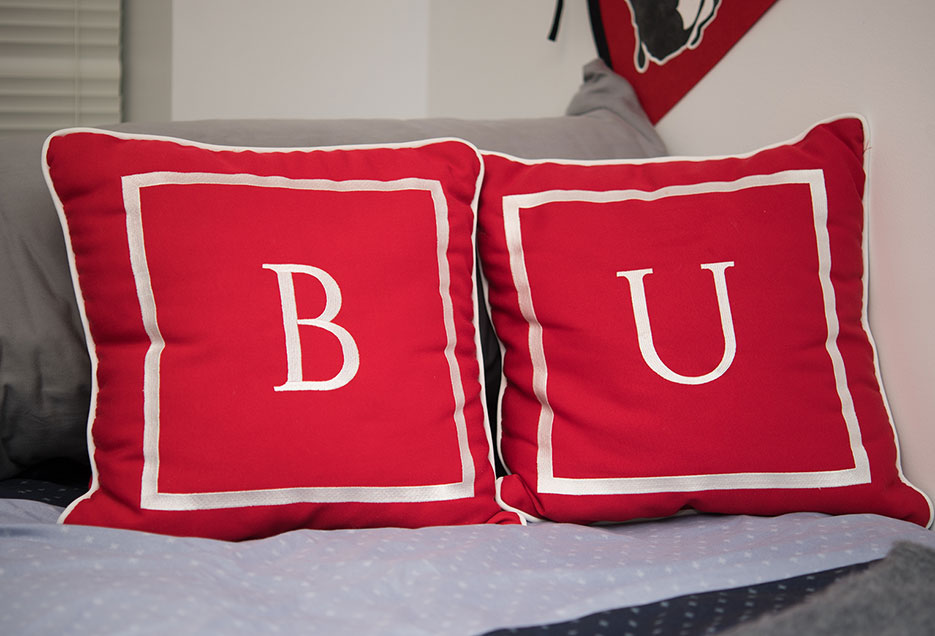 2 throw pillows spelling 'BU' on a dorm room bed.