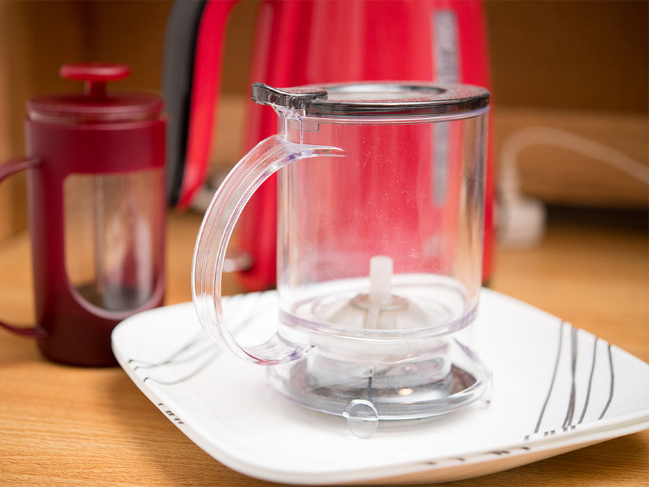 An electric kettle, coffee press, and tea steaper rest on a desktop.