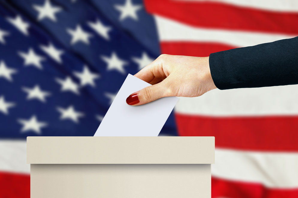 woman places ballot in voting box in front of an american flag