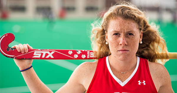 Portrait of Ally Hammel, Boston University Terriers field hockey NFHCA All-American, wearing her BU jersey and holding her stick on her shoulders.