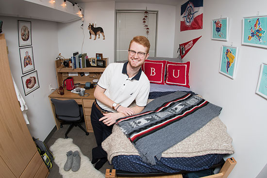 BU student Evan Dann stands smiling in his dorm room.