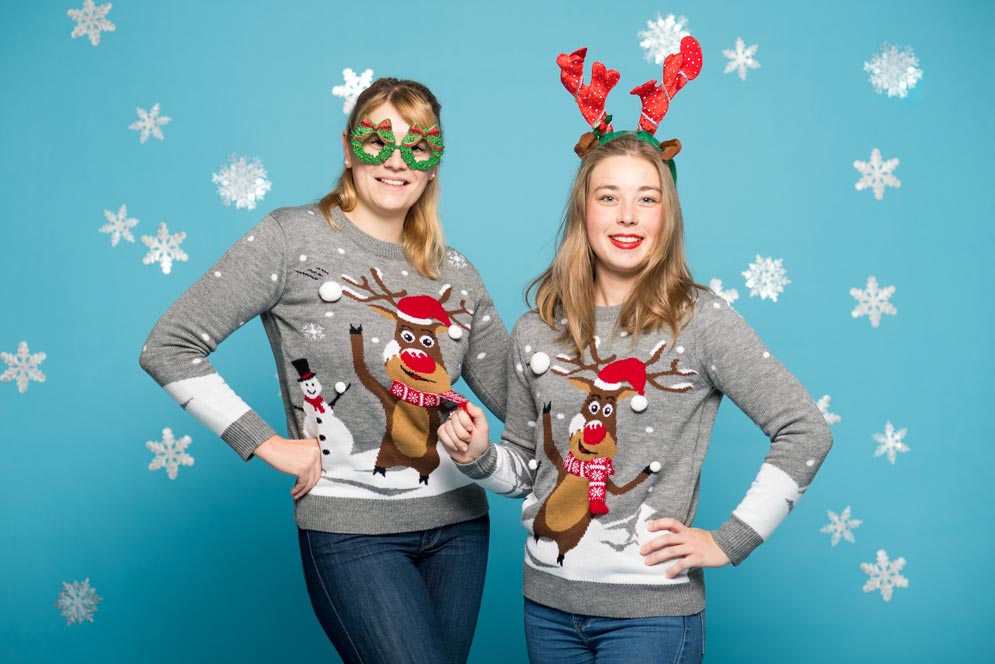 two girls pose in matching sweaters with a reindeer
