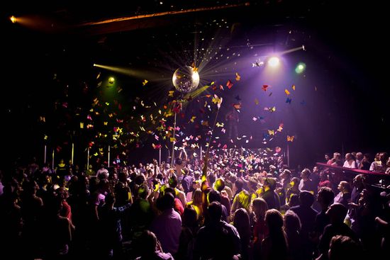 People dance in a room with a disco ball and paper butterflies