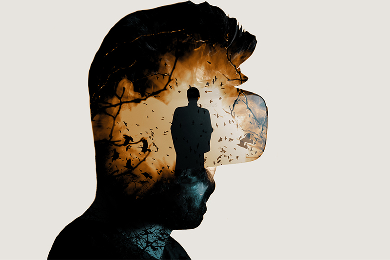 Double Exposure image of a man wearing Oculus Rift virutal reality goggles with nightmarish visions of a dark figure walking towards him out of a fiery forest background inside his head