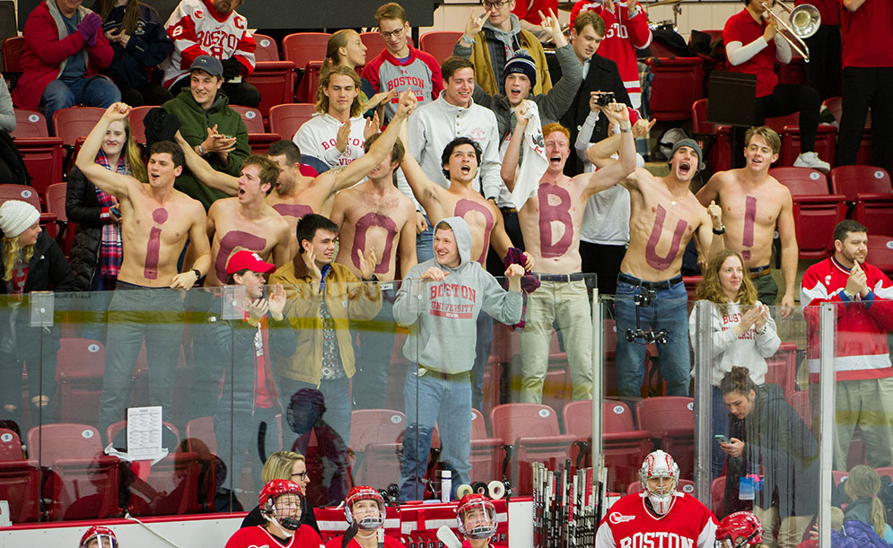 Boston University hockey fans celebrate the Terriers first goal of the game, some shirtless with the message GOOOBU! painted on their chests.