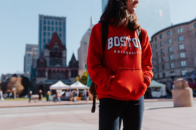 A Boston University student wearing a BU sweatshirt stands in Copley Square.
