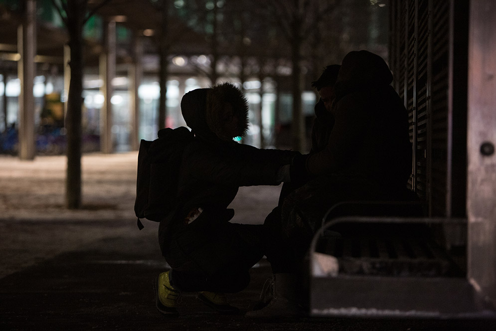 BU student Andrea Detorre kneels in front of a homeless couple sitting on a bus stop bench near Government Center trying to keep them warm as they await transport to a nearby shelter.