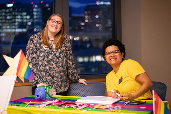 Therese Clover and Avery Ofoje pose behind a table covered in rainbows