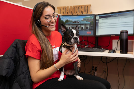 Antonietta holds boston terrier Rhett while sitting at a call center desk