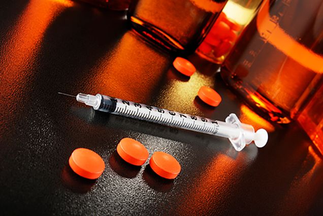 Drug addiction concept photo showing a syringe, pills and pill bottle on a black table.