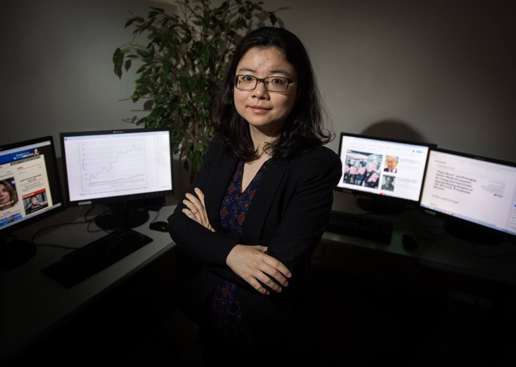Lei Guo, a COM assistant professor of emerging media studies, poses in front of four desktop screens.