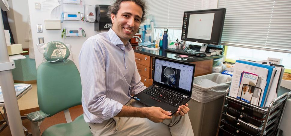 BU orthodontist Melih Motro sits on a dentist chair displaying an orthodontic x-ray on his laptop.