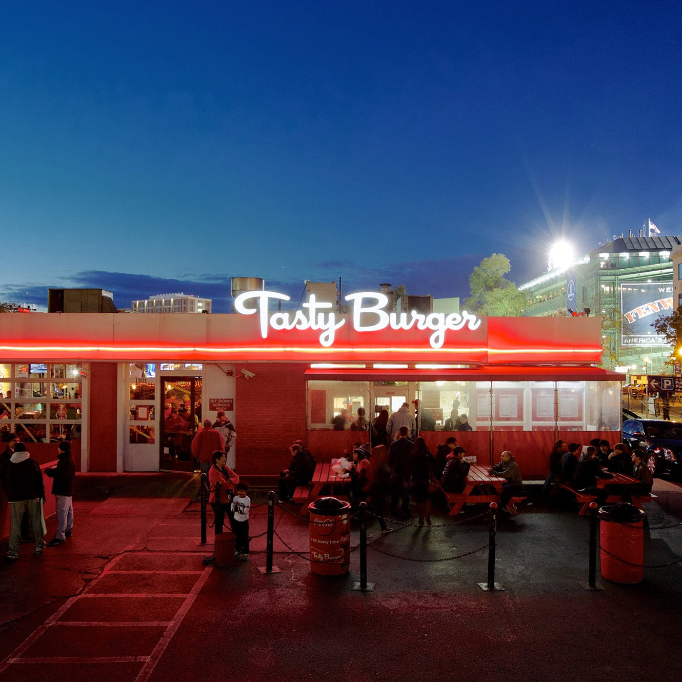 Photo of Tasty Burger at dusk. The neon sign sits on top of a single story building with a red neon trim.