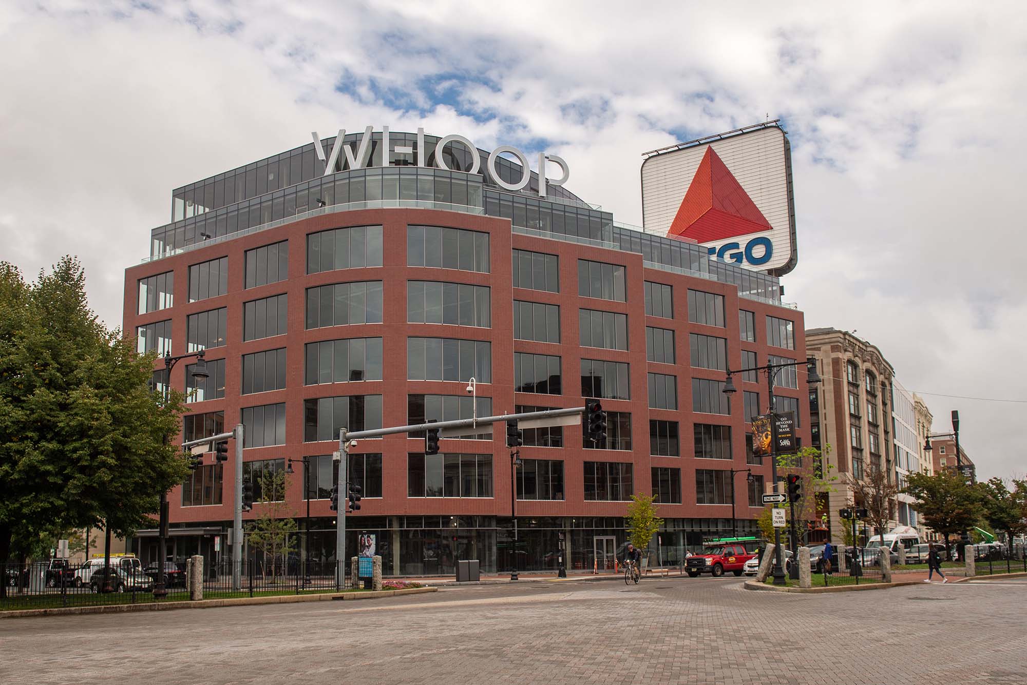 Photo of the multi-use building that is also the WHOOP headquarters in Kenmore Square. The building is brick with large blueish windows. A large grey "WHOOP" sign is prominent atop. A large CITGO sign can be seen peeking from behind the building.