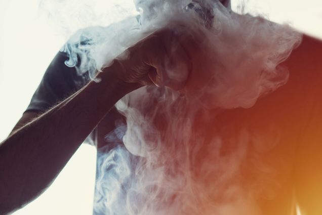 A teenager takes a hit from vaping e-cigarette blowing a cloud of vapor.