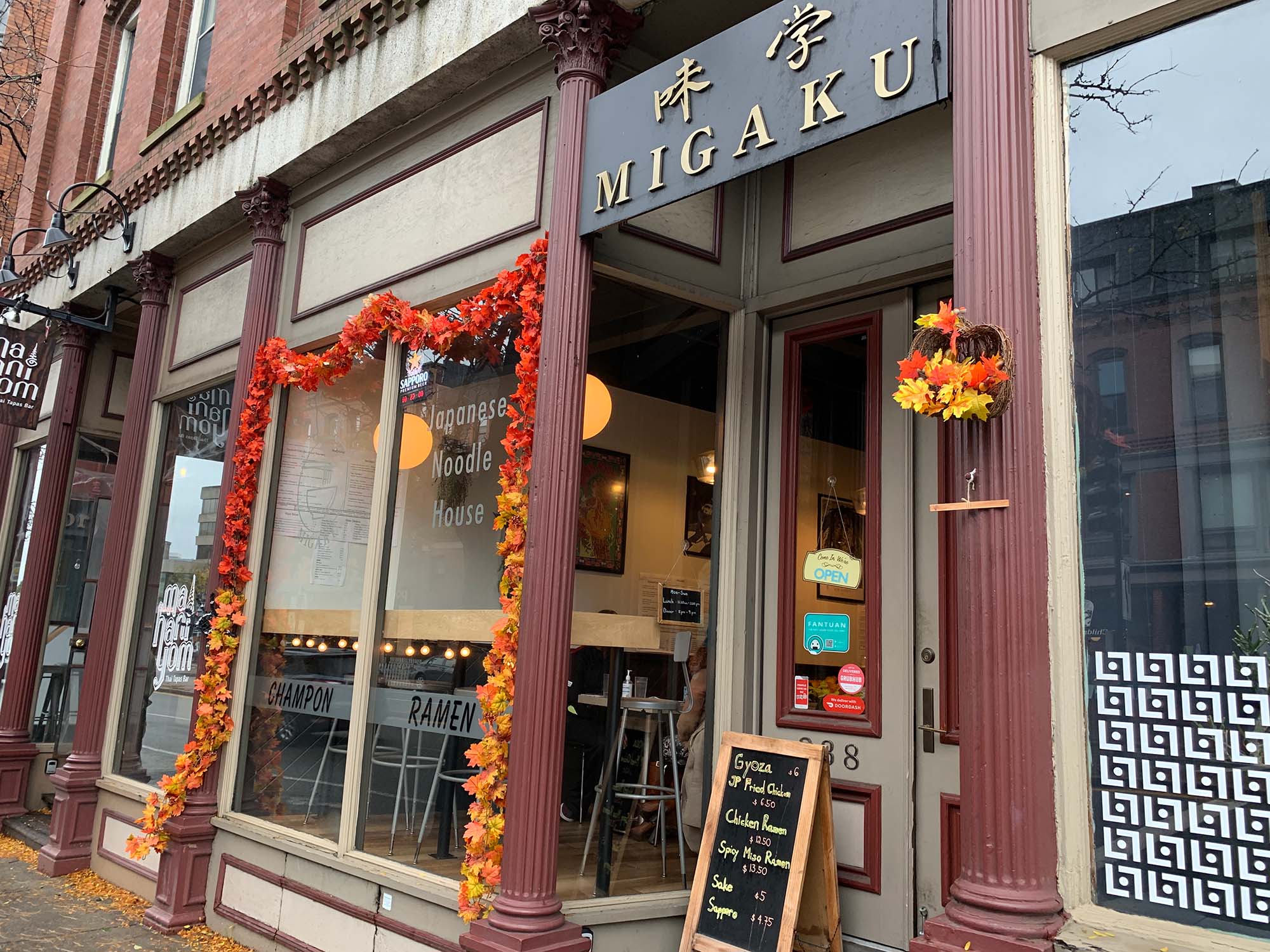 Photo of the exterior of Migaku Noodle House. Fake fall leaves line one of the windows.