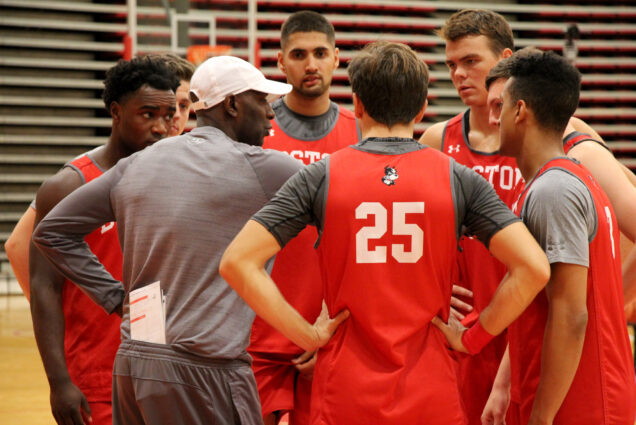Men's basketball team huddles up around their coach during practice